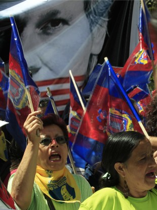 Demonstrators shout slogans as they hold up flags of the city of Quito in front of a Julian Assange poster during yesterday's march.