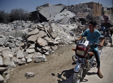 Syrians on motorcycles look at the damage of a destroyed house after it was hit by an air strike killing six Syrians in town of Tal Rifat on the outskirts of Aleppo city, Syria, Wednesday, Aug. 8, 2012
