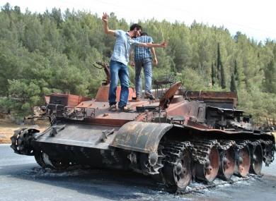 A Syrian man flashes the victory sign as he stands with his friend atop of a burned Syrian military tank which was destroyed during a clashes between Syrian forces and rebels in Saraqeb.