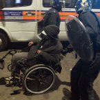A man in a wheelchair is helped by riot police in Tottenham, north London as trouble flared after members of the community took to the streets last night to demand justice, after Mark Duggan, 29, was shot dead by police.