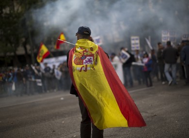 A police officer wearing a Spanish flag walks in front of a demonstration where other police officers protest by blocking the street in front of the Interior Ministry in Madrid, Spain, Saturday, Oct. 27, 2012.
