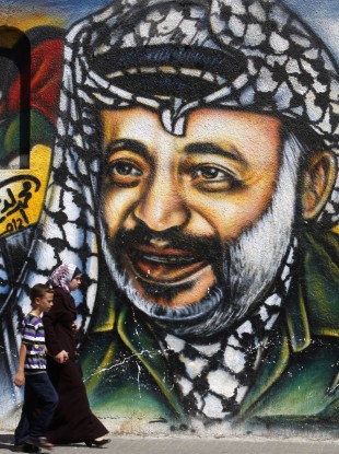 Palestinians pass by a mural depicting late Palestinian President Yasser Arafat, in Gaza City