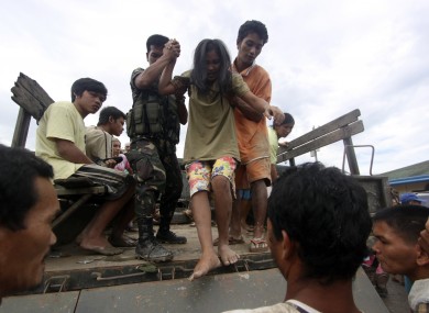 A resident who was rescued from her flooded home is assisted as she alights from a military truck in New Bataan, Compostela Valley province, southern Philippines