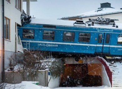 The derailed train hangs on the edge of the track after it crashed into the side of a residential building in Saltsjobaden outside Stockholm, Sweden.